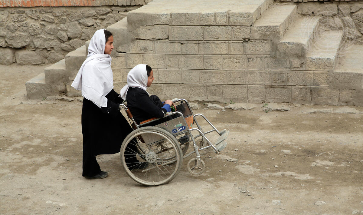 Una niña lleva a otra niña en silla de ruedas.