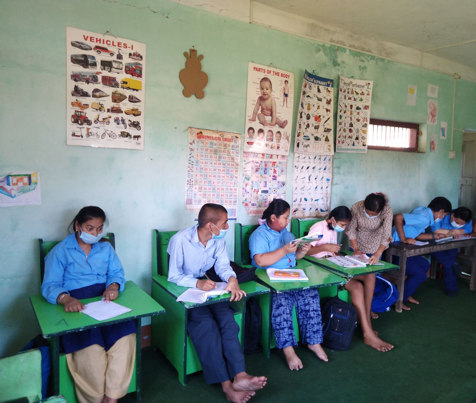 elever vid PFPID dagcenter i nepal sitter i skolbänkar med munskydd under en lektion