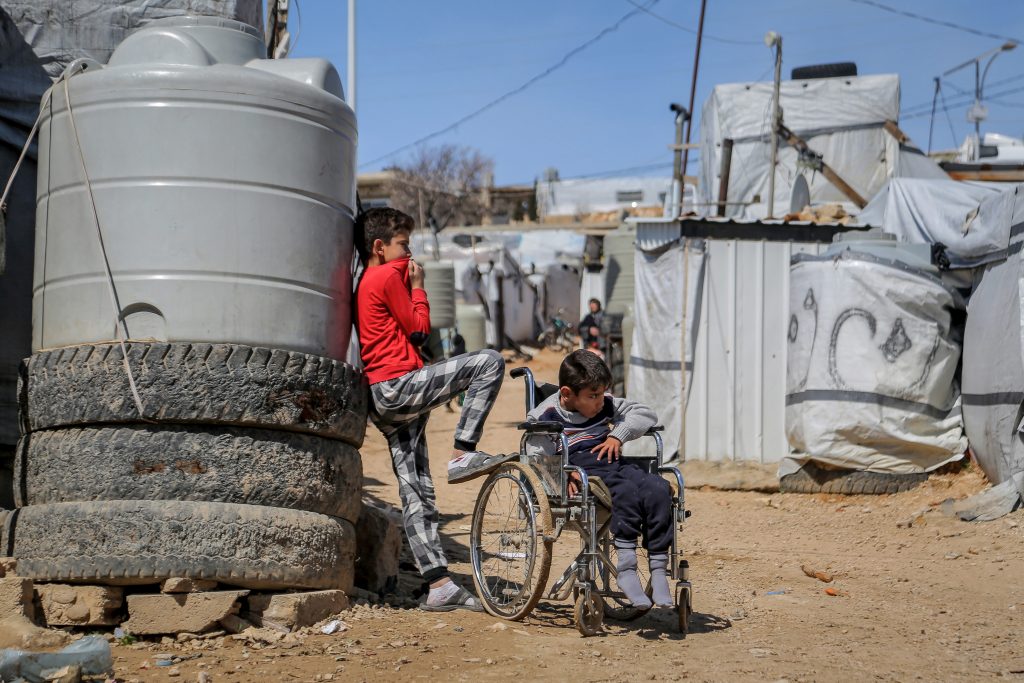 dječak sjedi u invalidskim kolicima pored njega stoji brate oni su u izbjegličkom kampu