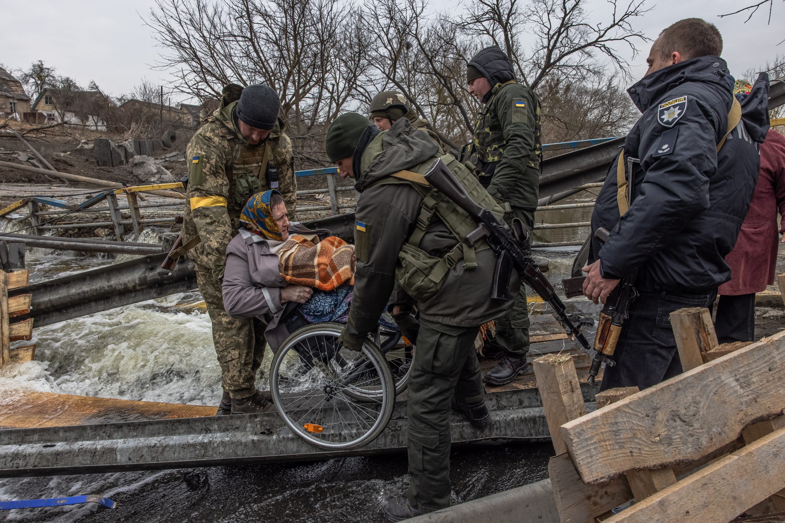 Una mujer en silla de ruedas es transportada por soldados a través de un puente destruido en Kiev, Ucrania.
