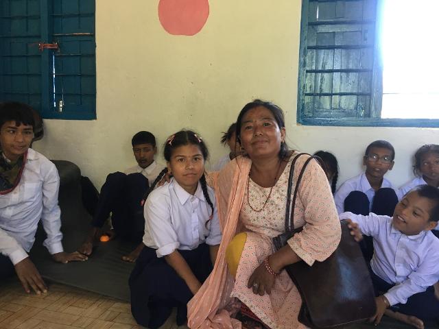 Indira sits next to her daughter in a school room, they smile at the camera.