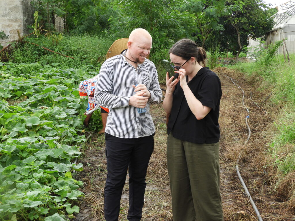 Erika och en medlem från TAS står i ett grönsaksland och pratar. Erika läser på sin mobil.