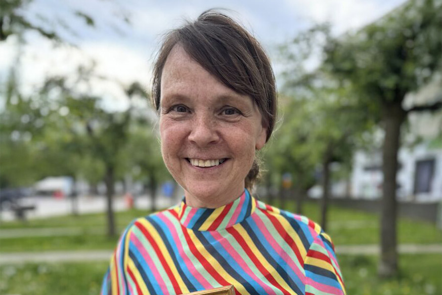 Mariann har mörkt uppsatt hår och en randig färggrann tröja.